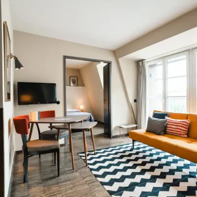 Sofa und Sitzecke in Suite im HENRI Hamburg Gelbes Sofa vor einer Fensterfront und Tisch mit zwei Stühlen