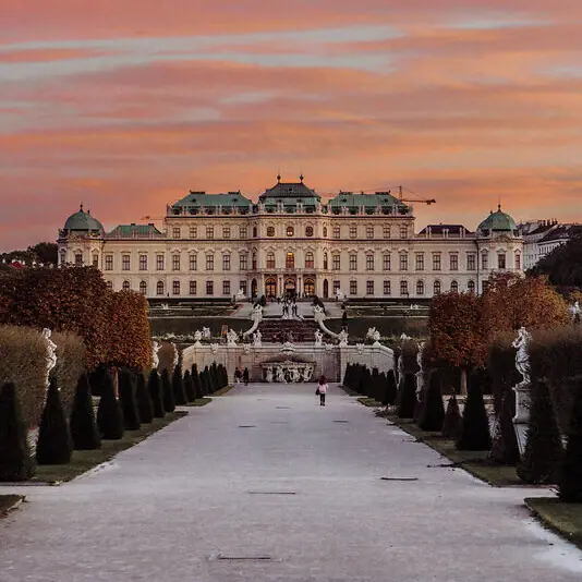 Schloss Belvedere Ein großes weißes Gebäude mit einem Gehweg und Bäumen.
