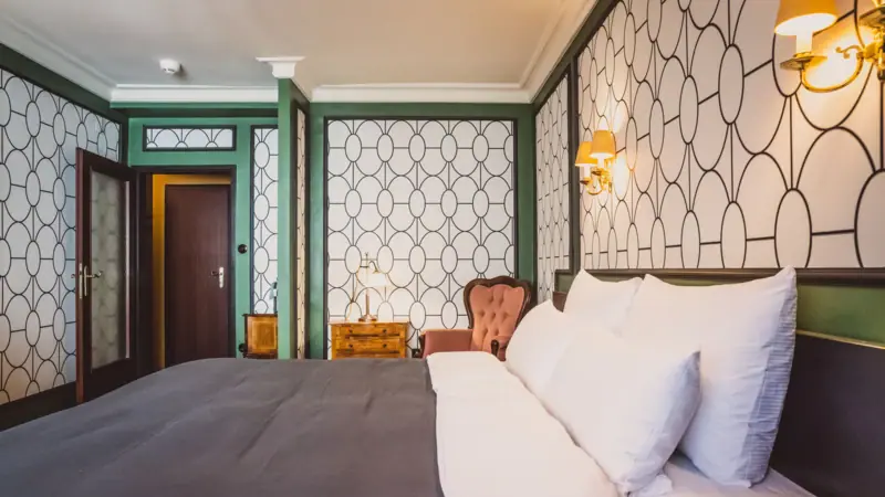 Zimmeransicht Ein Bett mit Kissen und einem Stuhl in einem Zimmer.