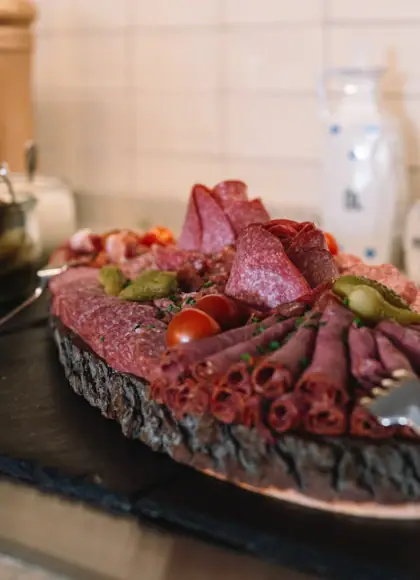 Lecker und regional Rustic wooden platter with a variety of sliced cured meats, presented on a wooden table alongside bread and cutlery.
