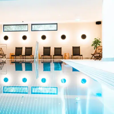 Indoor Swimmingpool im HENRI Hotel Kitzbühel Ein Swimmingpool mit Treppen und Liegestühlen.