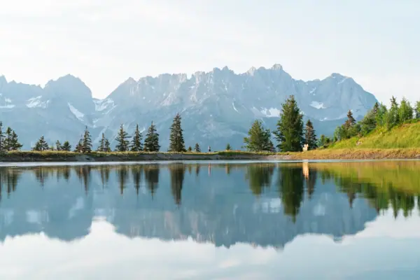 Astbergsee mit Bäumen und Bergen im Hintergrund