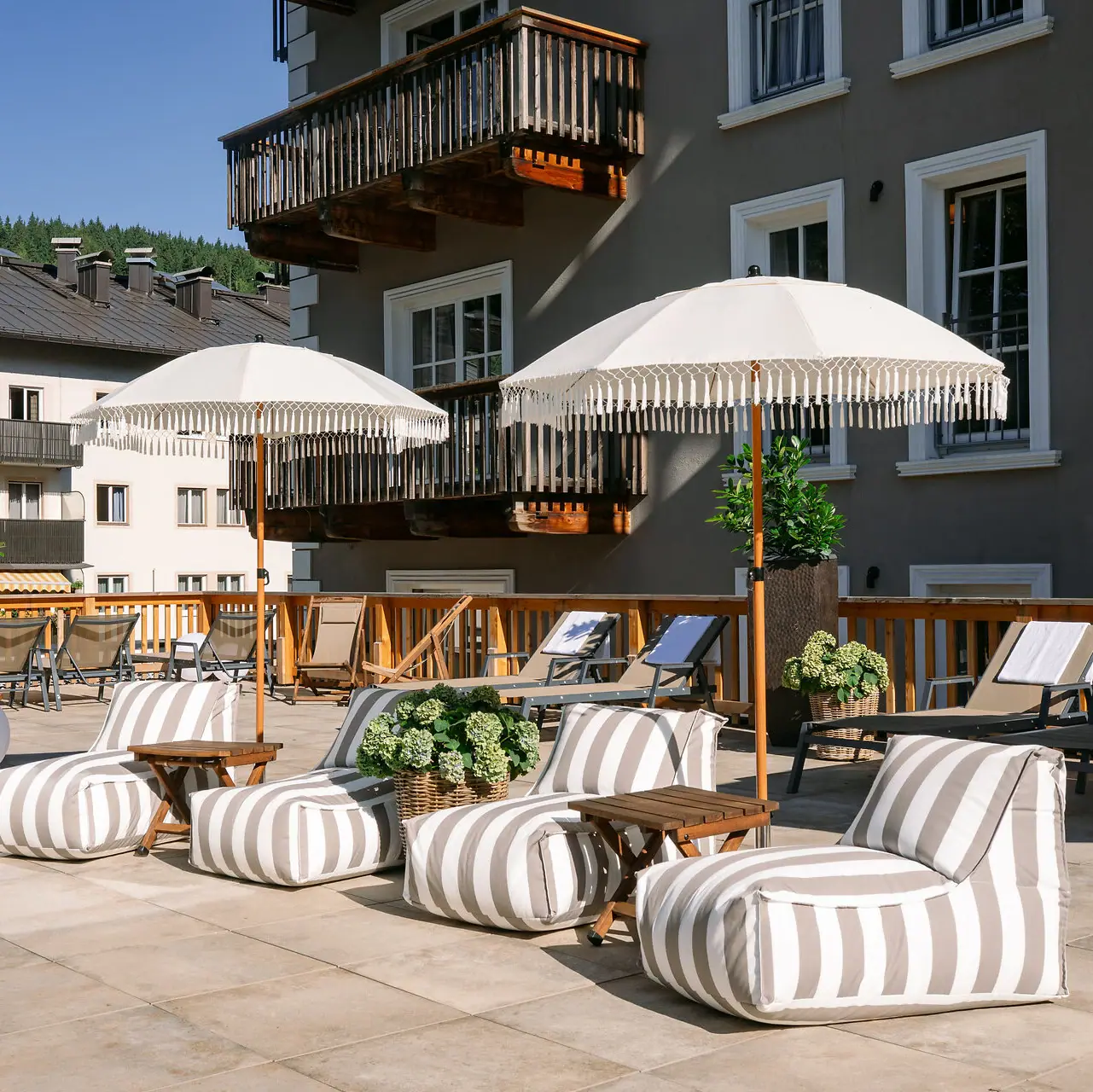Sonnenterrasse des HENRI Hotels Kitzbühel Ein Patio mit Stühlen und Sonnenschirmen.