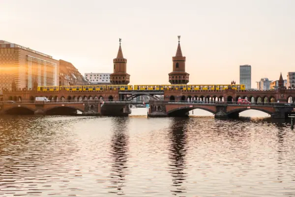 Oberbaumbruecke-Berlin-Spree-Sonnenuntergang Ansicht der backsteingotischen Oberbaumbrücke in Berlin bei Sonnenuntergang mit einer gelben U-Bahn und Spiegelung im Wasser.