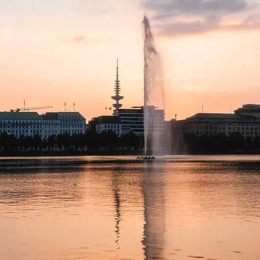 Alster Springbrunnen in einem Gewässer mit Gebäuden im Hintergrund.