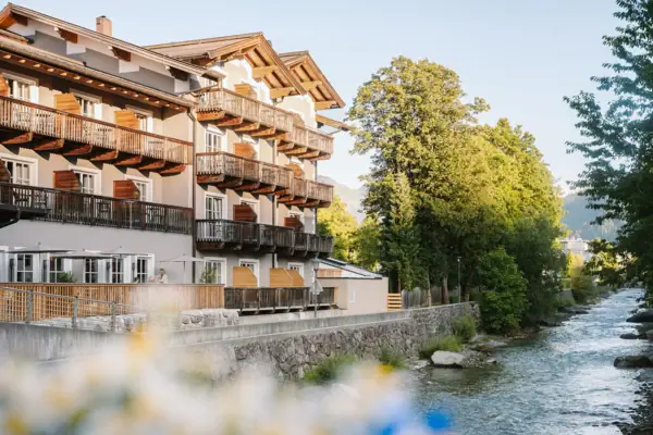 HENRI Kitzbühel Außenansicht Ein Gebäude mit Balkonen und einem Fluss im Vordergrund.