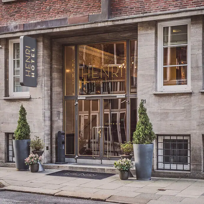 Eingang HENRI Hotel Hamburg Ein Gebäude mit Glastüren und einem Schild.