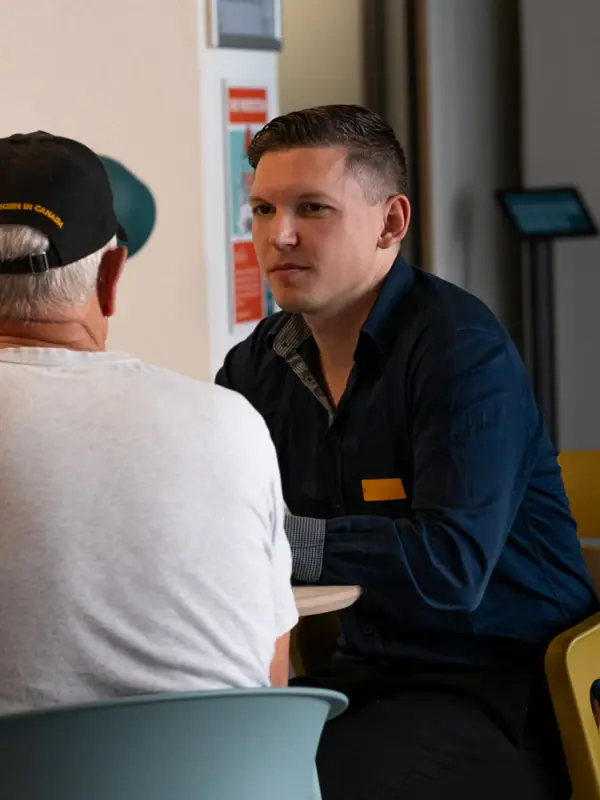 Coworking Space Ein Mann sitzt mit einem anderen Mann im weißen Hemd an einem Tisch.