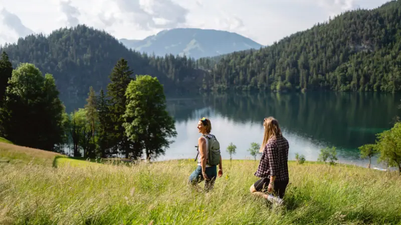 Zwei Personen stehen in einem grasbewachsenen Feld an einem See.