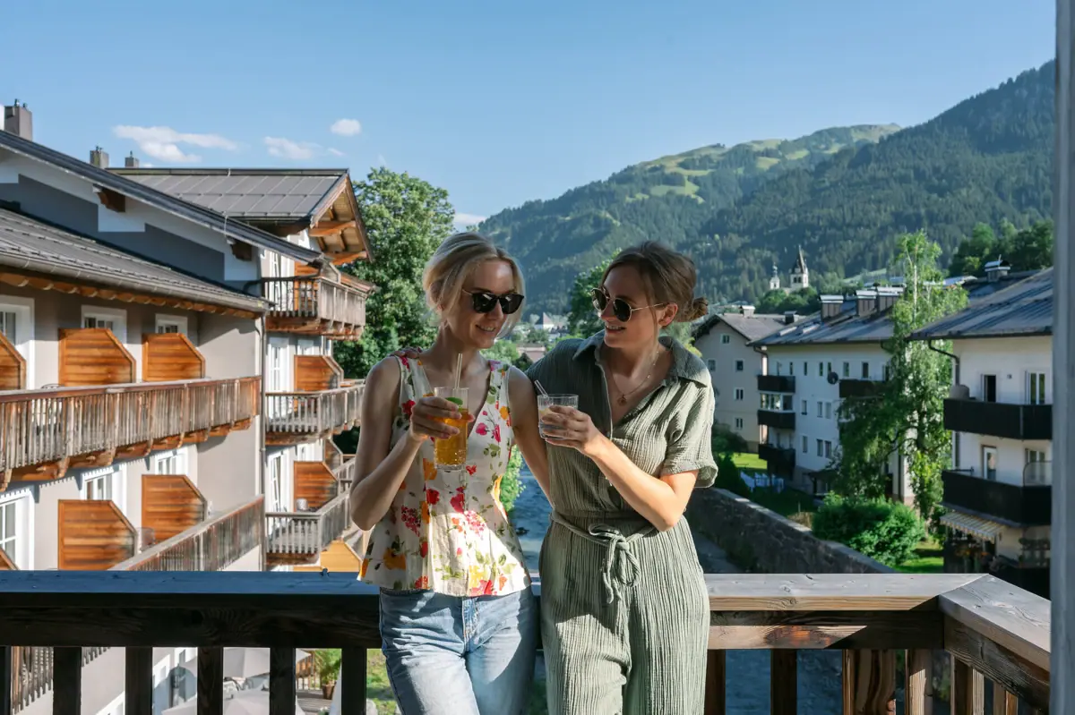 Zwei Frauen stehen auf einem Balkon mit Blick auf Berge und Bäume.