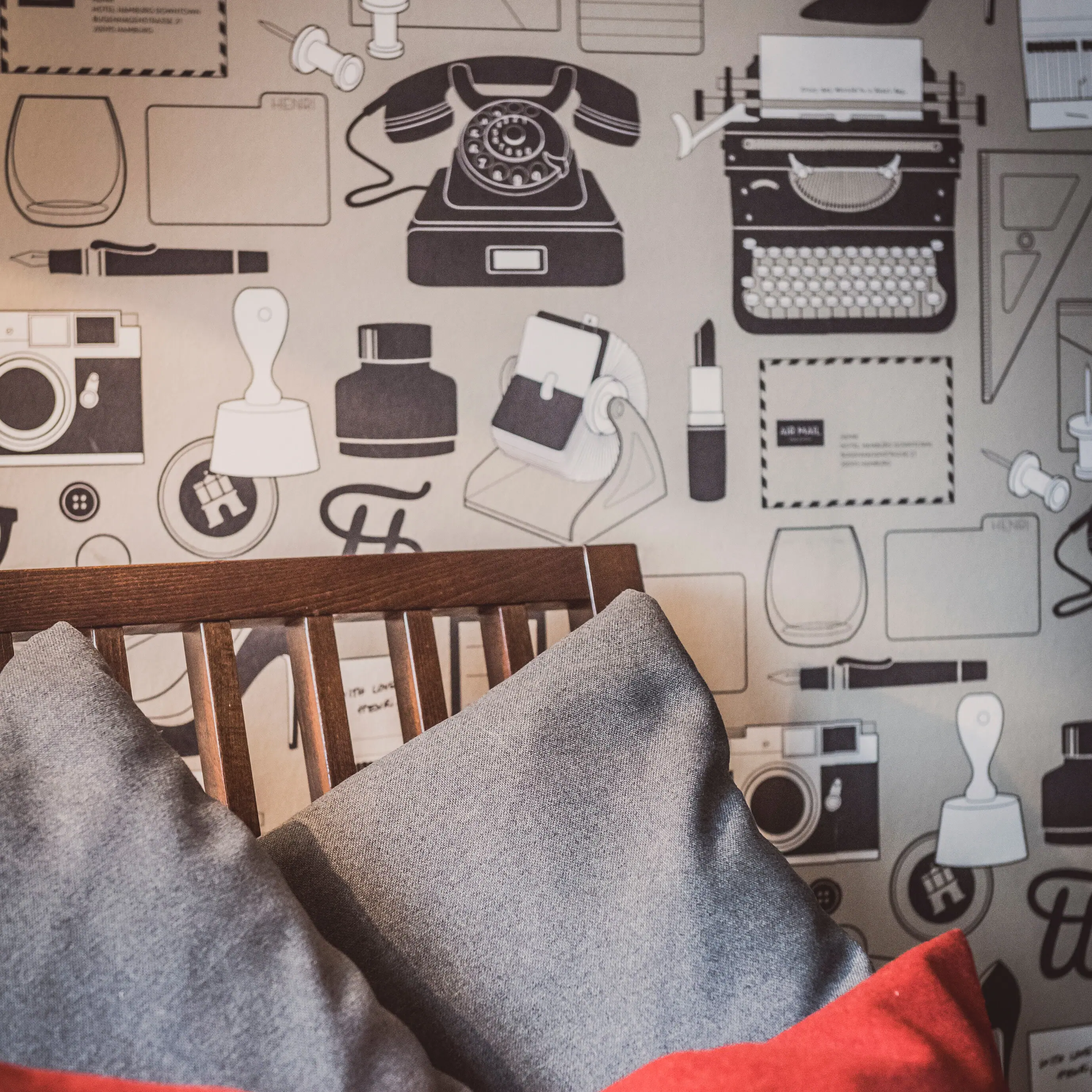 Sessel mit Kissen vor einer Wand Sessel mit grauen und roten Kissen vor einer Wand mit Motivtapete