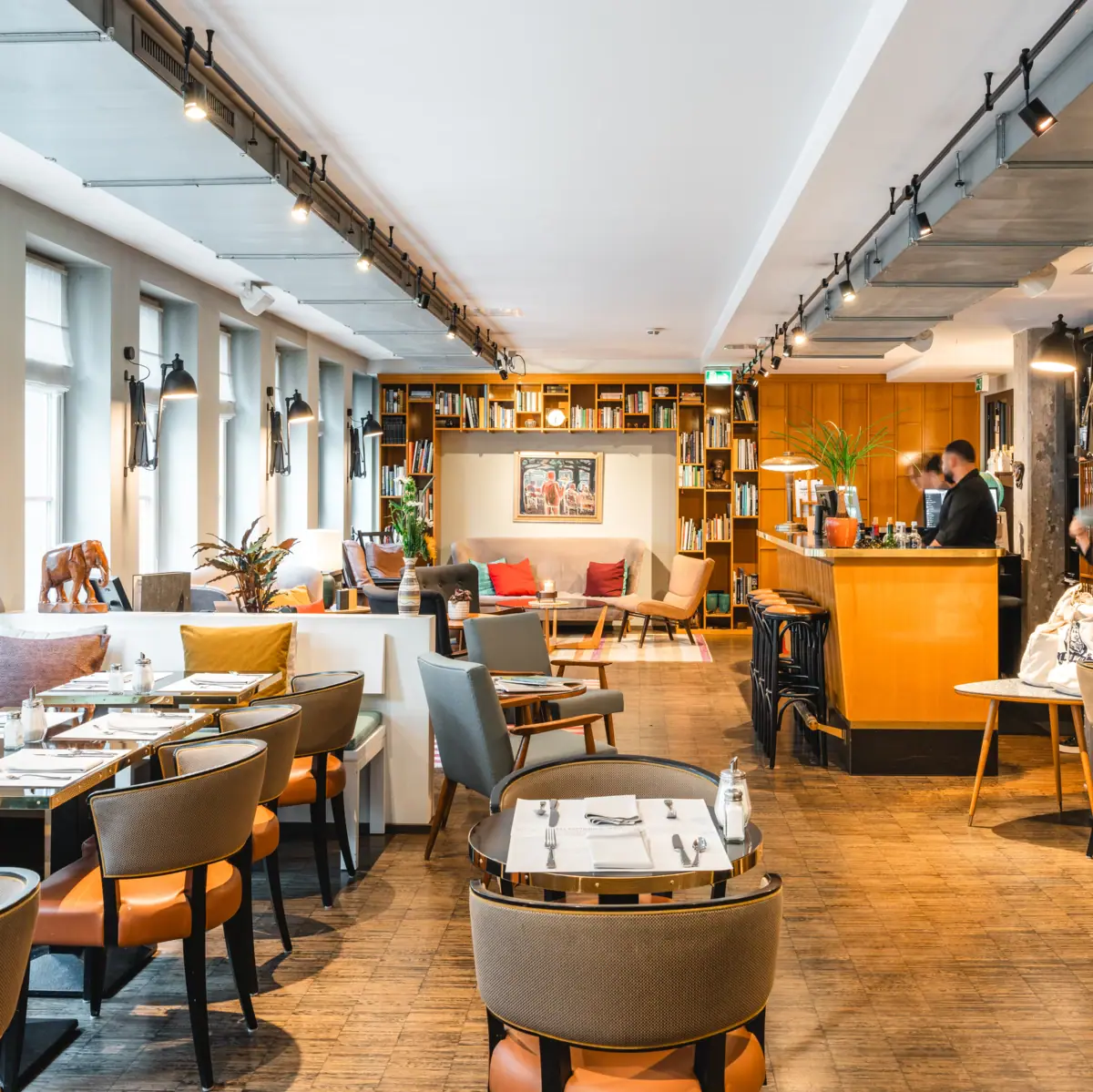 Kontorküche und Lounge im HENRI Hotel Hamburg Einladender Loungebereich mit vielen Tischen, Stühlen und Bänken.