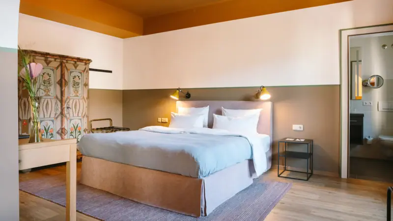 Hotelzimmer im HENRI Garmisch-Partenkirchen Ein Hotelzimmer im HENRI Garmisch-Partenkirchen mit einem großen gemütlichen bett, einem alten Schrank und einer Tür zum angrenzenden Badezimmer.