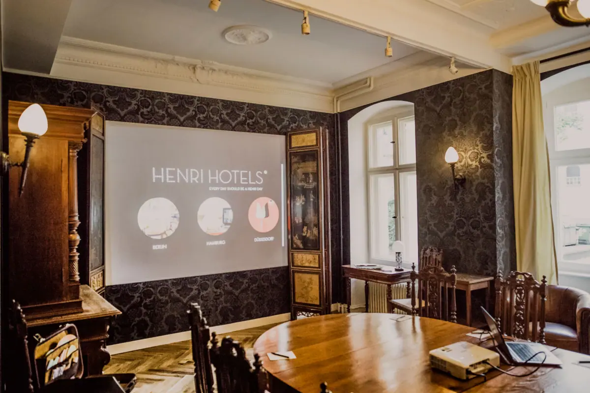 HENRI Berlin Tagungsraum Ein Zimmer mit Leinwand und Möbeln.