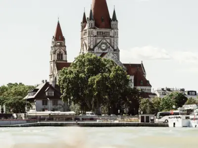 Ab 65 € pro Person im Doppelzimmer mit Frühstück Bauwerk mit Turm und Uhrenanzeige neben Bäumen am Wasser.