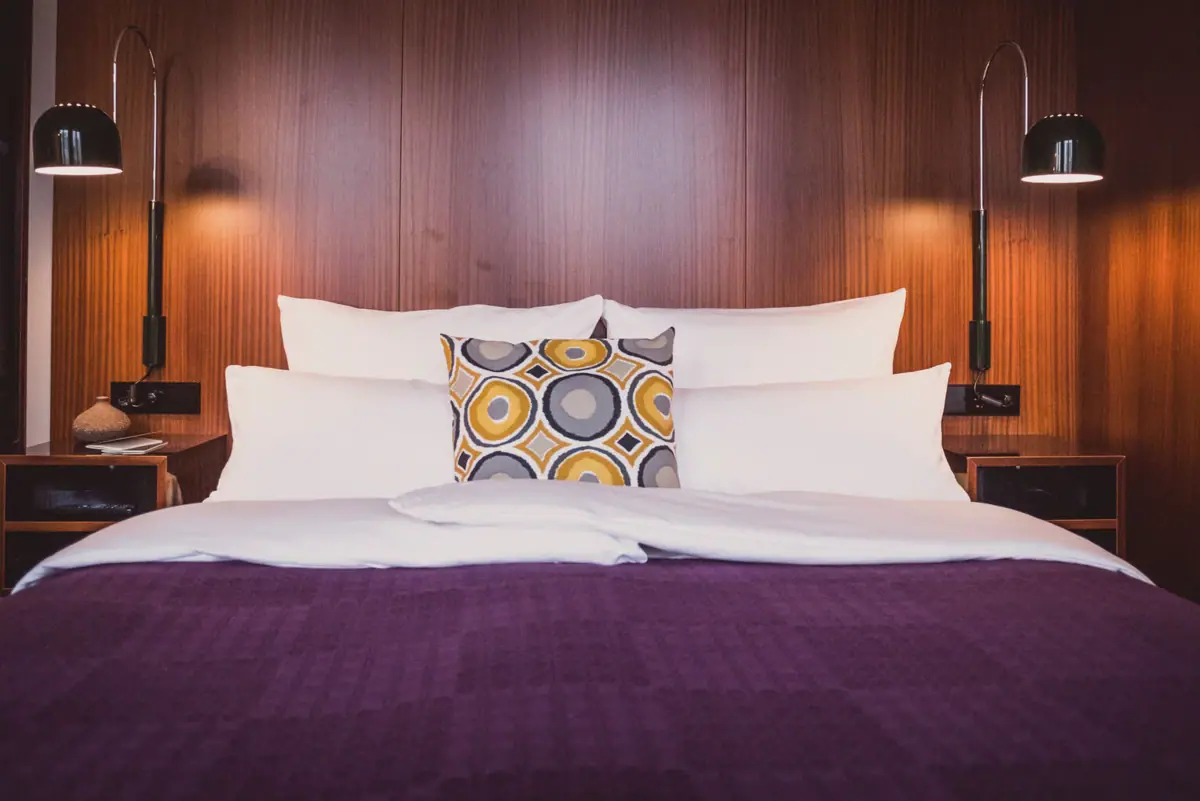 Zimmer im HENRI Hotel Düsseldorf Ein Bett mit Kissen und einer Lampe.