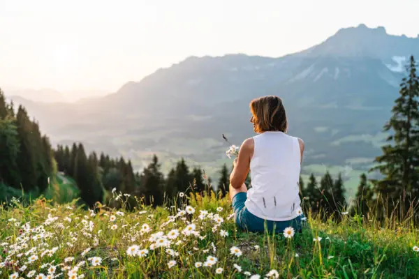 Frau sitzt in den Bergen Eine Frau sitzt auf einem Hügel mit Blumen.
