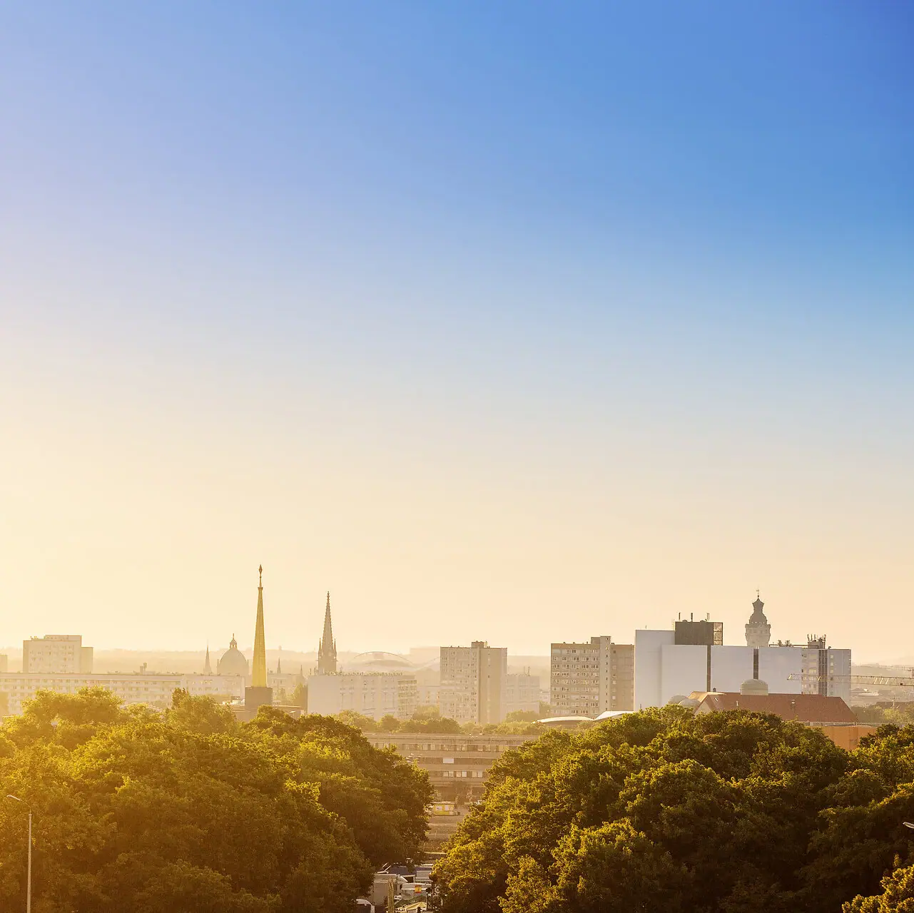 Leipzig Stadt-Skyline mit Bäumen im Vordergrund und klarem Himmel im Hintergrund.