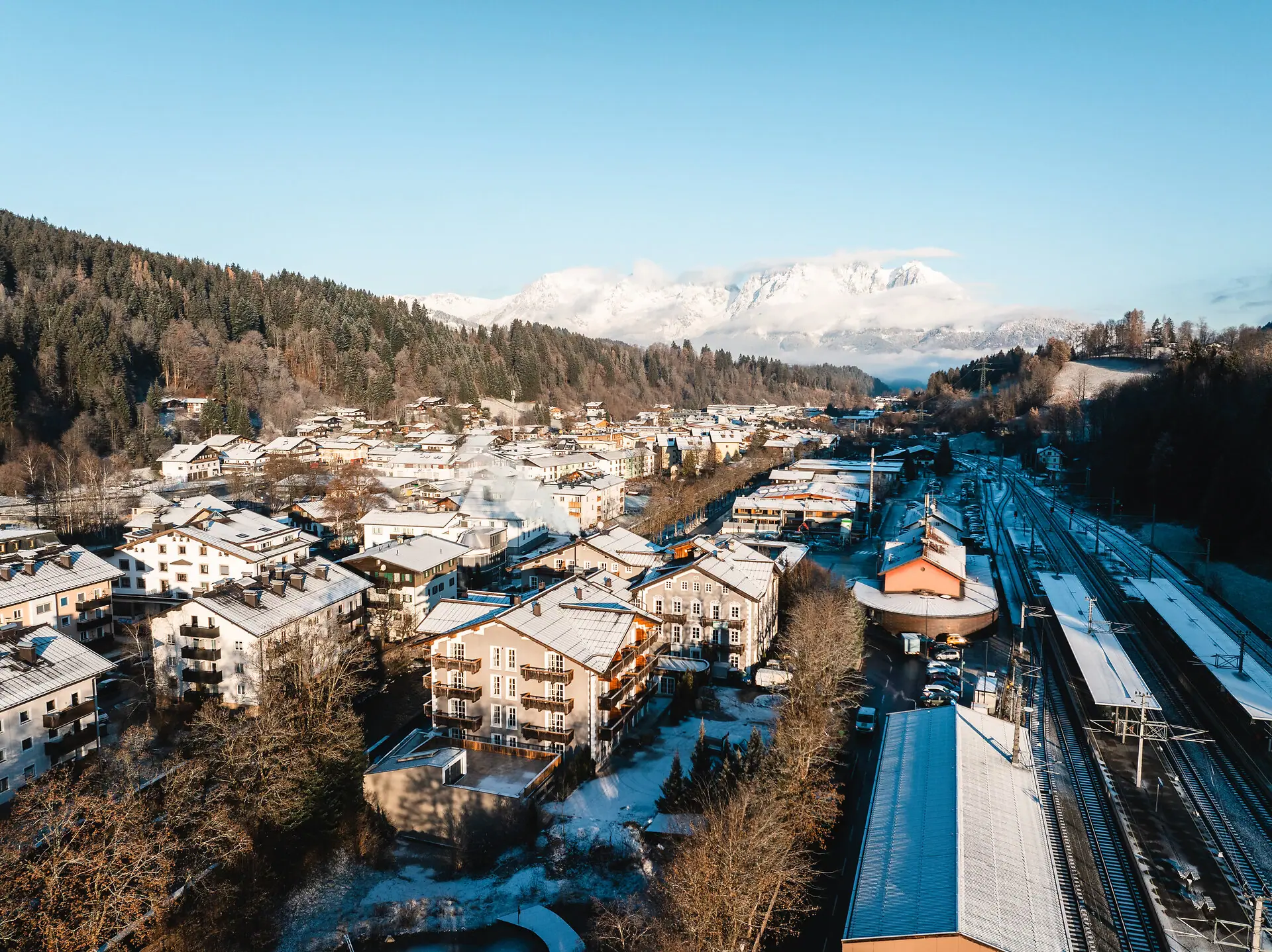 HENRI Kitzbühel Drohnenansicht Eine verschneite Stadt im Winter mit Bergen im Hintergrund.