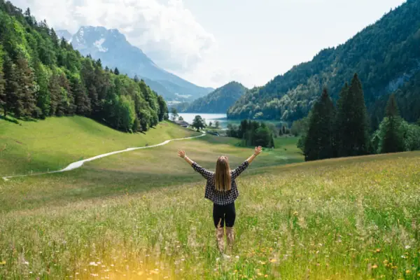Kitzbühel Ausblick Berge Frau steht mit erhobenen Armen in einem Feld mit Bergen im Hintergrund.