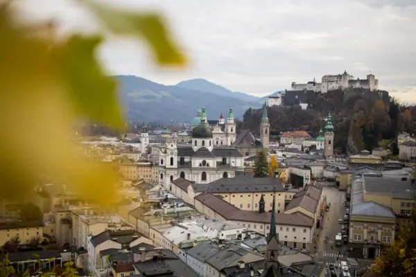 Salzburg Eine Stadt mit vielen Gebäuden und einem Hügel mit Bäumen und Bergen im Hintergrund.