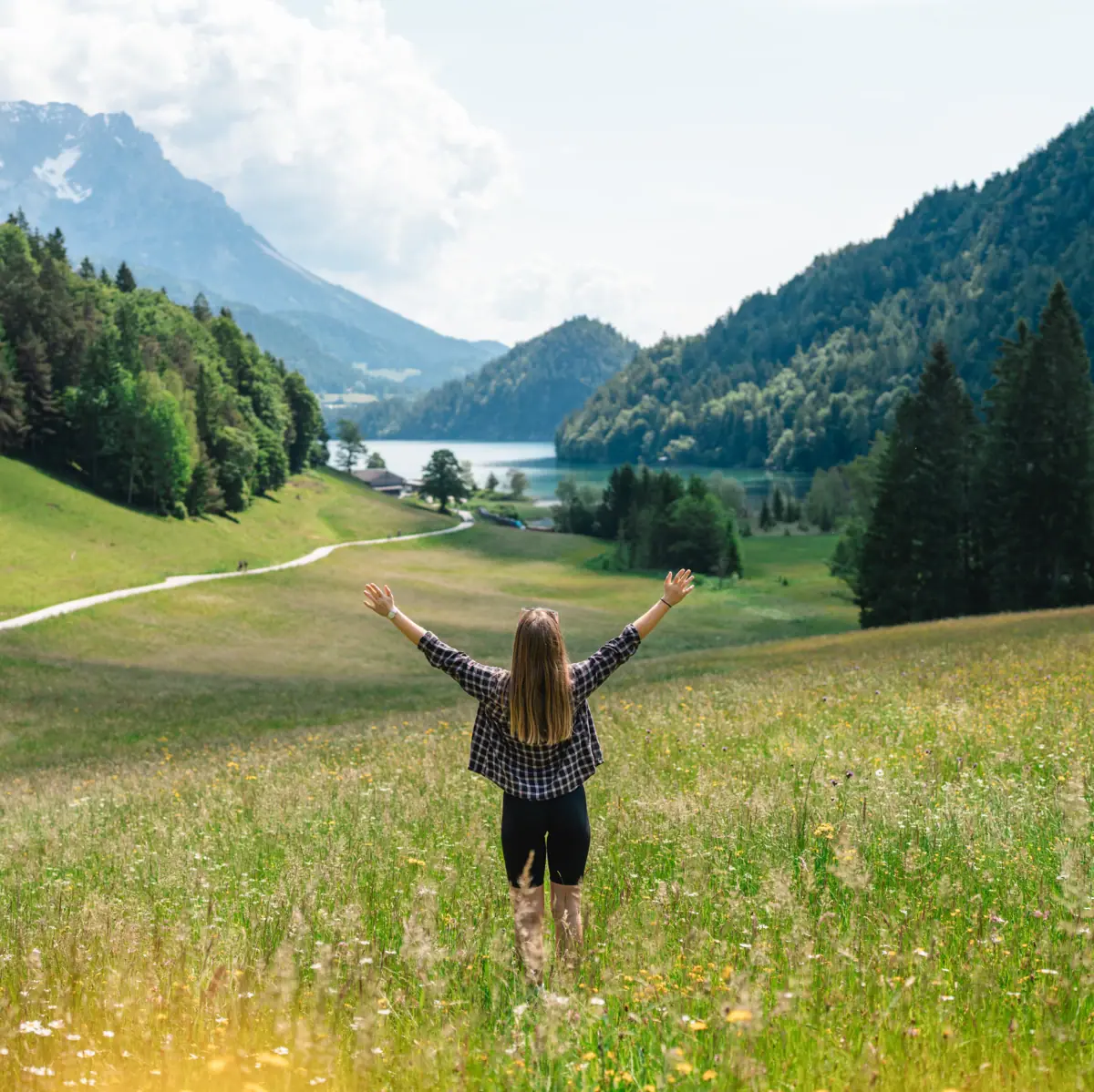 Kitzbüheler Alpen Eine Frau steht in einem Feld und streckt die Arme in die Höhe und im Hintergrund sind Berge zu sehen.