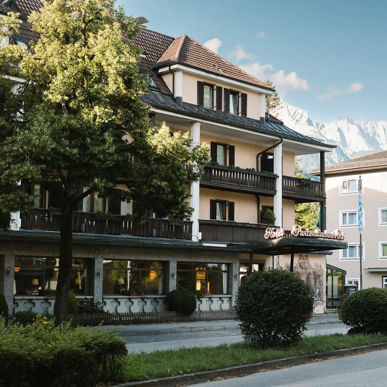 HENRI Hotel Garmisch-Partenkirchen Ein Gebäude mit Bäumen und Büschen am Straßenrand.