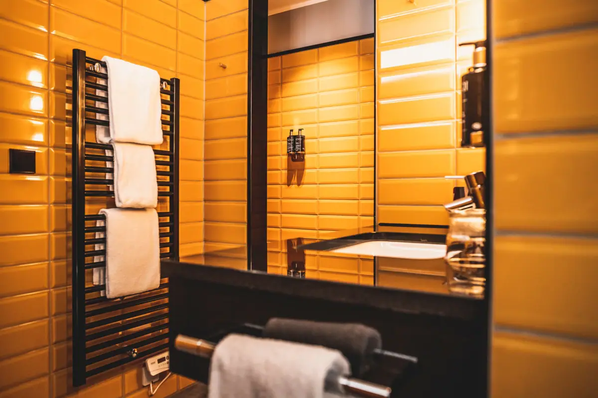 Badezimmer im HENRI Hotel Düsseldorf Badezimmer mit gelben Fliesenwänden und einem Spiegel