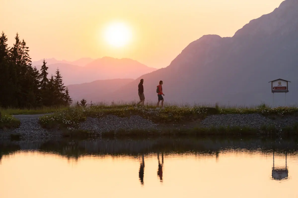 Sonnenuntergang vor Bergsee Zwei Personen spazieren auf einem Hügel an einem See.