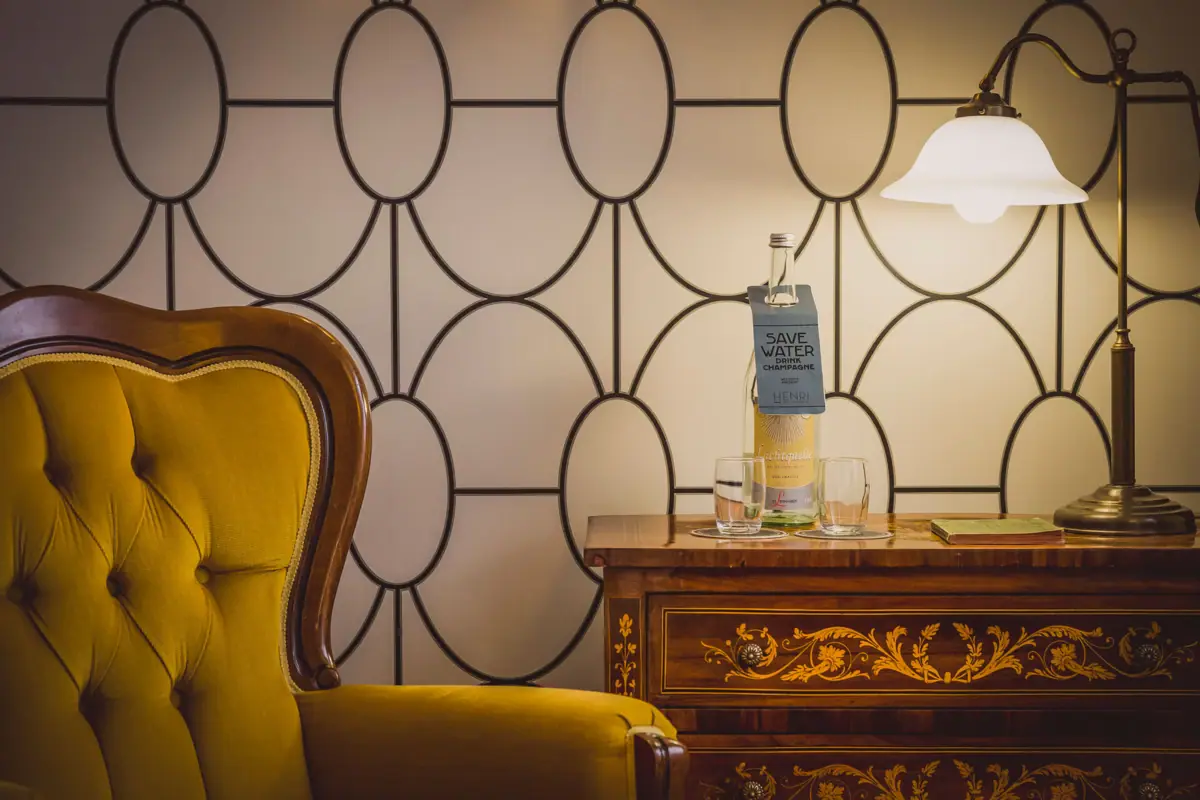 Zimmerdetail Ein Stuhl und ein Tisch mit Gläsern und einer Flasche darauf.