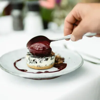 bhk Hand hält einen Löffel über ein Dessert.