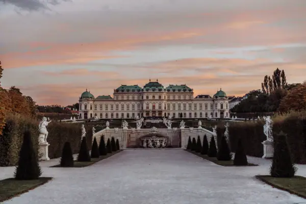 Schloss Belvedere Ein großes weißes Gebäude mit einem Brunnen und einem Gehweg im Vordergrund.