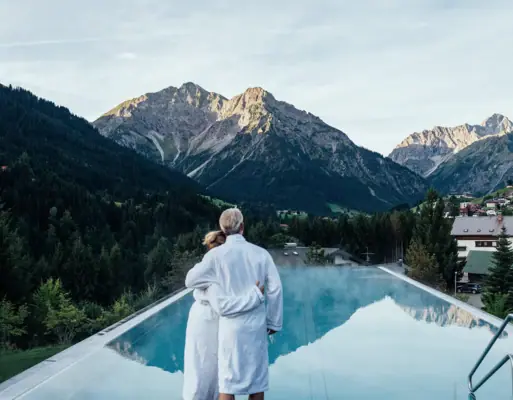 A-ROSA Ifen Hotel Kleinwalsertal Ausblick Pool Ein Mann und eine Frau stehen auf einem Pooldach mit Bergen im Hintergrund.