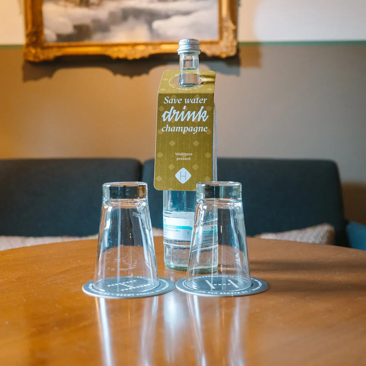 Wasserflasche im HENRI Hotelzimmer Eine Flasche und Gläser auf einem Tisch.