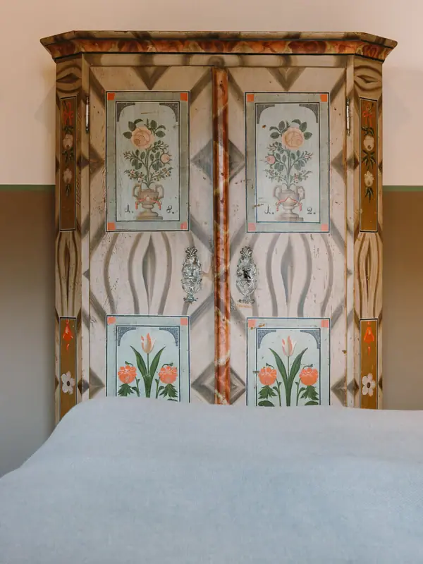 Alter Schrank HENRI Garmisch-Partenkirchen Ein Bett mit bemaltem Schrank im Hintergrund.