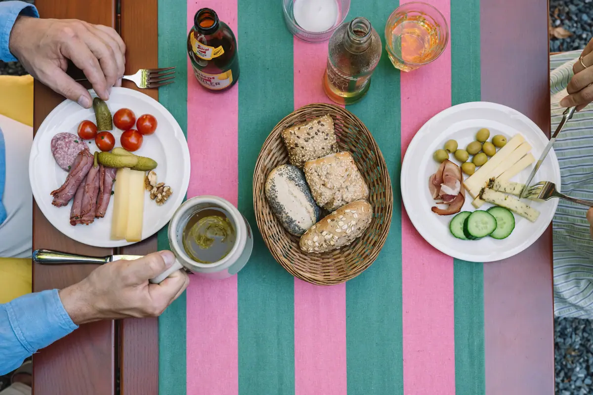 Tisch mit Essen Person hält eine Tasse und einen Teller mit Essen.