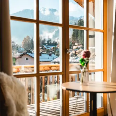 HENRI Kitzbühel Fenster mit Blick auf ein Bergpanorama und einer Blumenvase auf einem Tisch