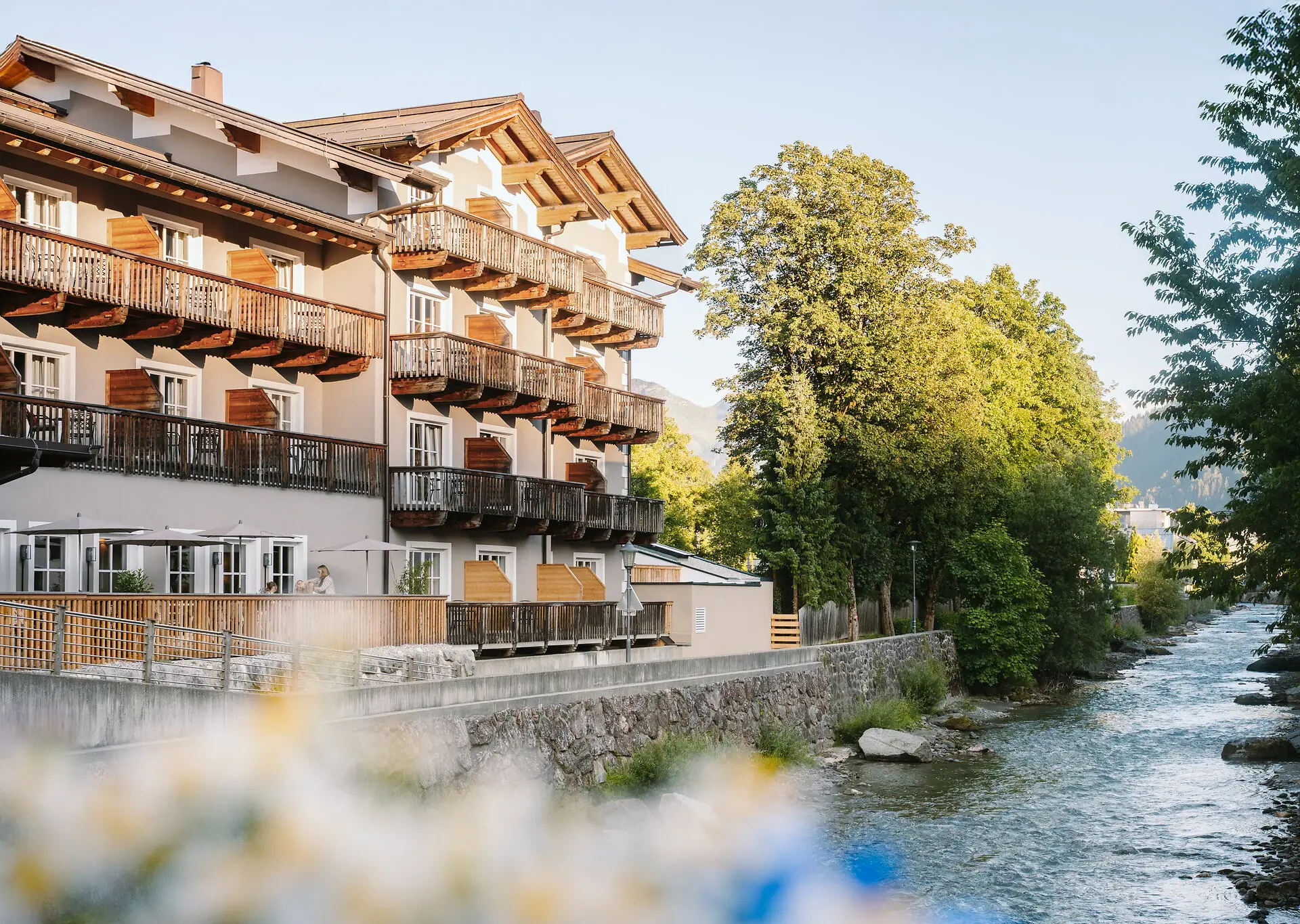 HENRI Kitzbühel Außenansicht Ein Gebäude mit Balkonen und einem Fluss im Vordergrund.