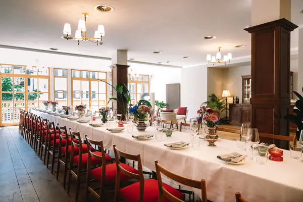 Salon Milano im HENRI Hotel Kitzbühel Langer Tisch mit weißen Tischdecken und roten Stühlen.