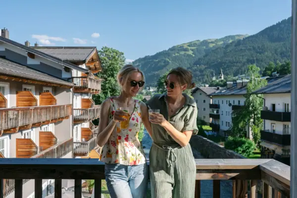Kitzbühel Zwei Frauen stehen auf einem Balkon mit Blick auf Berge und Bäume.