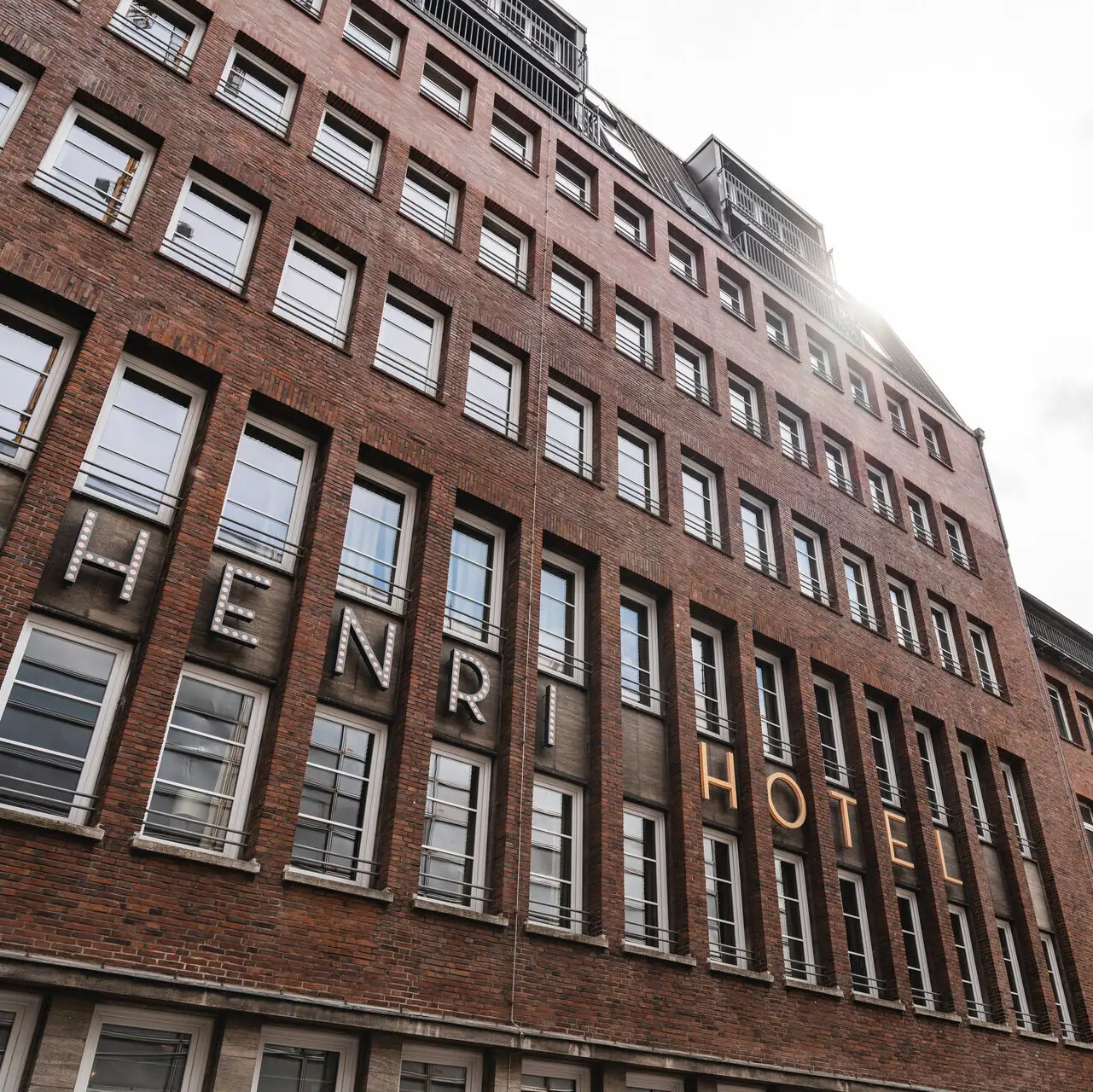 HENRI Hamburg Ein Gebäude mit einem hohen Turm vor bewölktem Himmel.