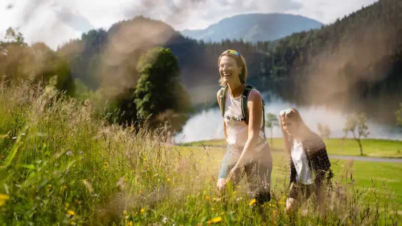 Wanderungen in der Natur von Kitzbühel Zwei Frauen in einem Feld mit Gras und Pflanzen unter freiem Himmel.