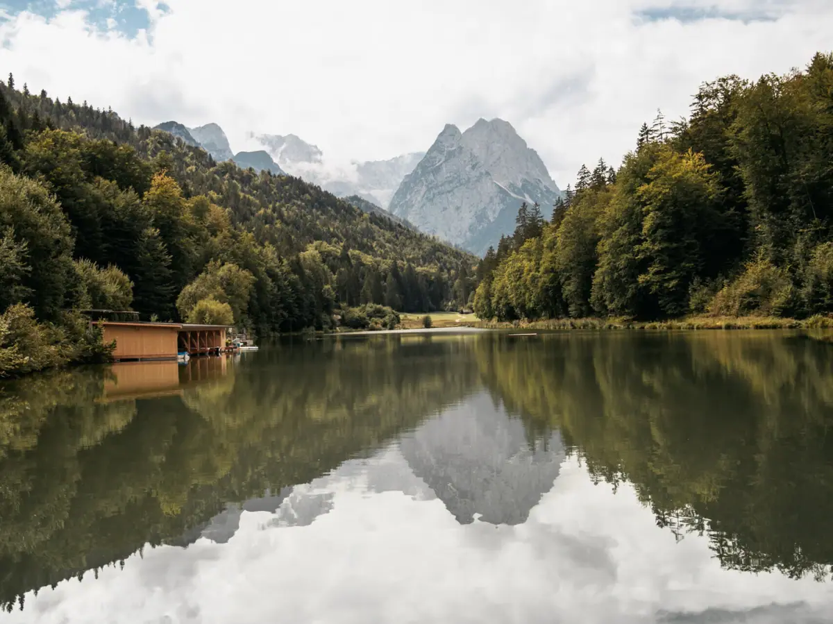 Riessersee Ein See mit einer Hütte und Bergen im Hintergrund.