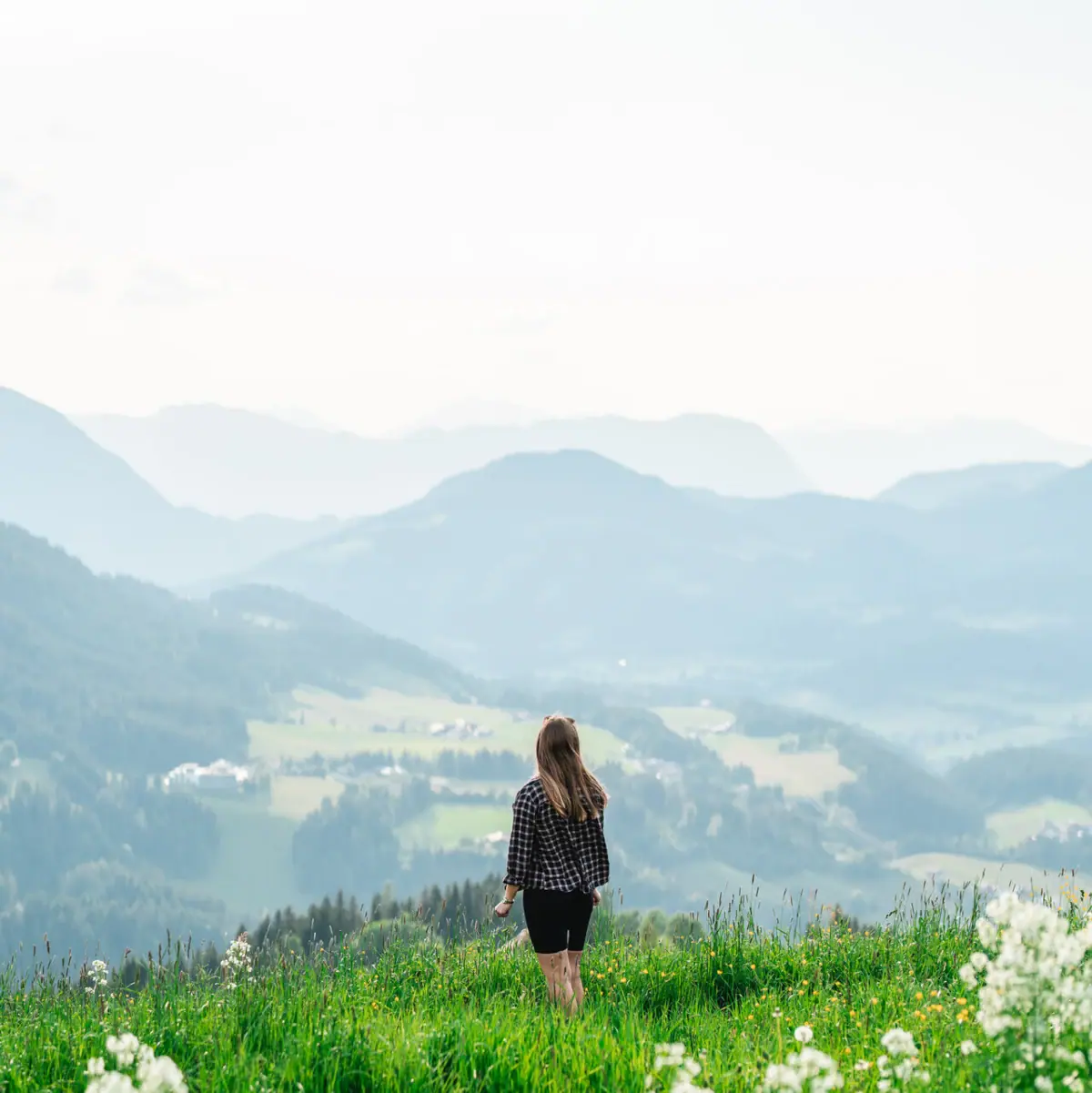 Frau steht in den Bergen Eine Frau steht auf einem grasbewachsenen Hügel mit Bergen im Hintergrund.