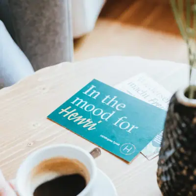 HENRI Gutschein Eine Person hält eine Tasse Kaffee.