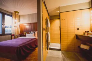 S-Studio HENRI Düsseldorf Das S-Studio im HENRI Hotel Düsseldorf mit einem Bett und einem angrenzendem Bad mit einem Waschbecken und einer Dusche.