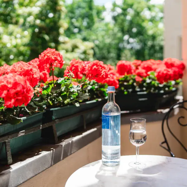 HENRI Hotel Berlin Balkon Eine Flasche und ein Glas Wasser auf einem Tisch mit roten Blumen.