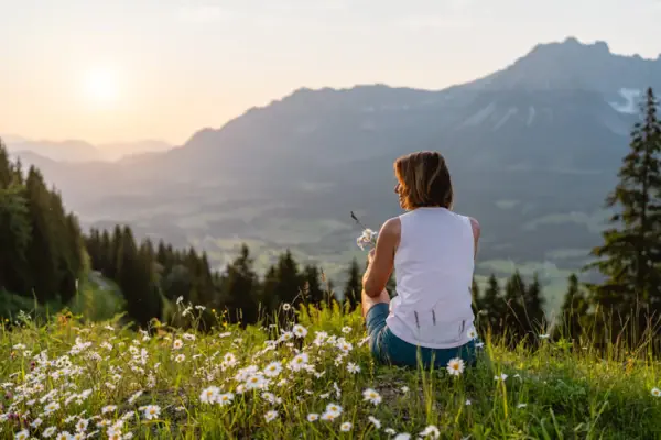 Blick aufs Alpenpanorama Eine Frau sitzt auf einem Hügel mit Blumen.