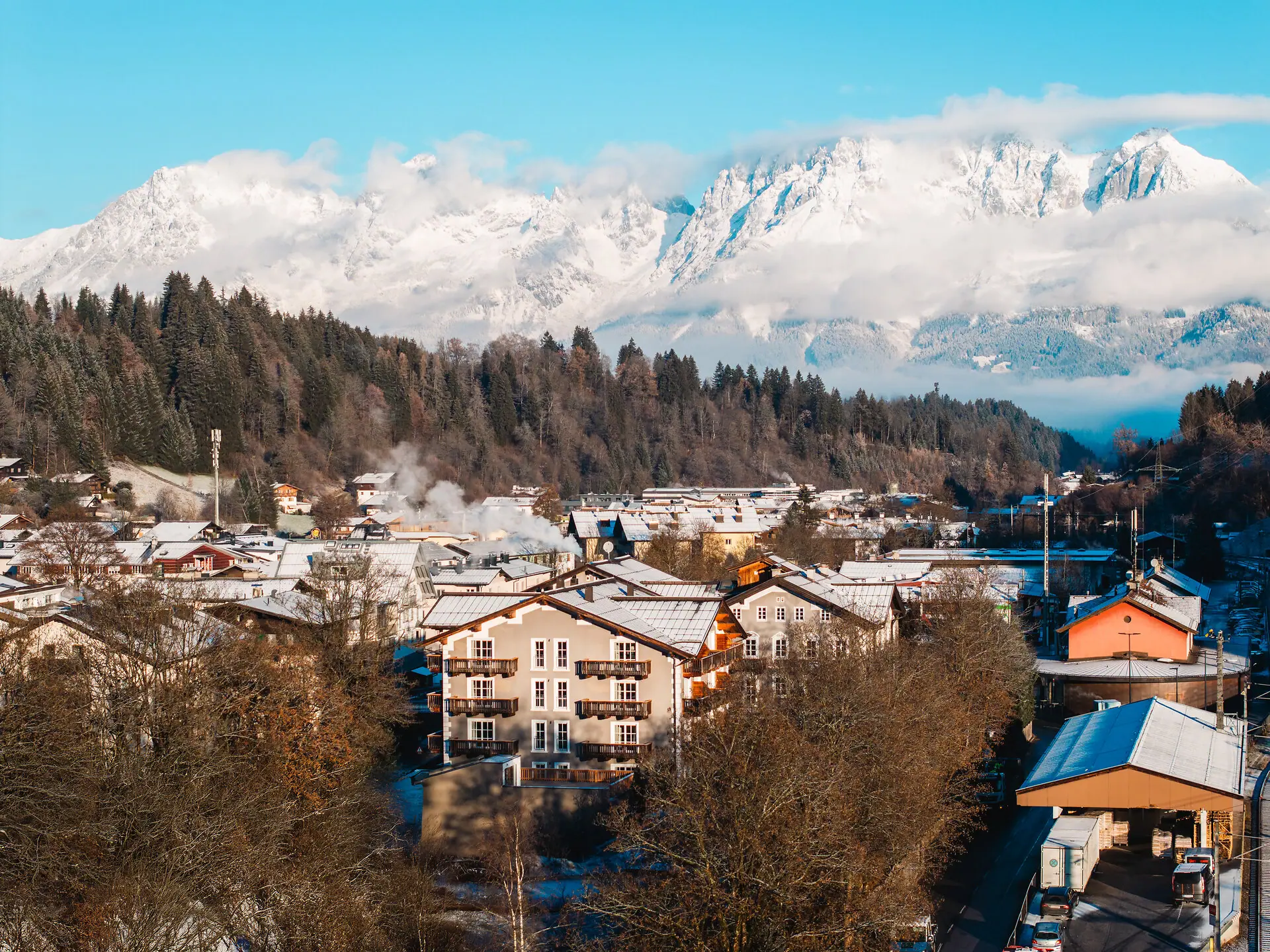HENRI Kitzbühel Drohnenansicht Ein Bergdorf mit schneebedeckten Bergen im Hintergrund.