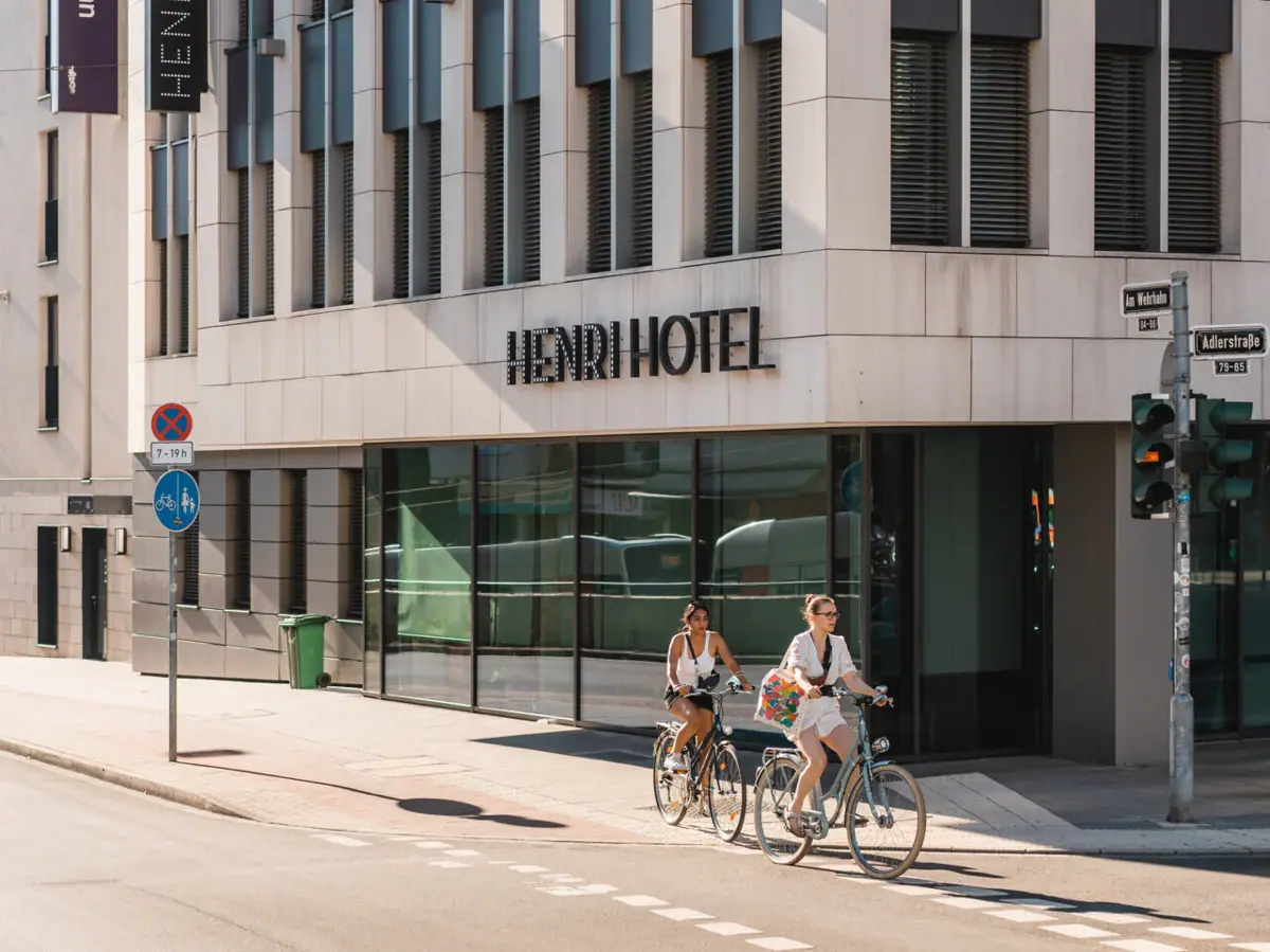 HENRI Hotel Düsseldorf Eine Gruppe von Menschen fährt mit Fahrrädern auf einer Straße vor einem Hotel.